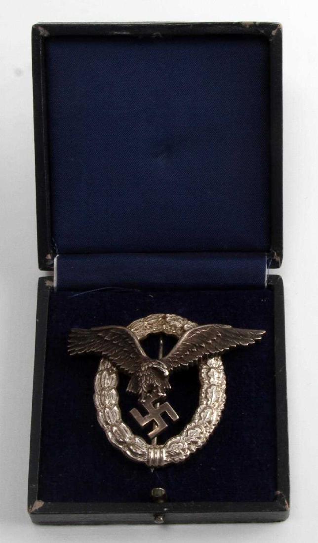 GERMAN WWII LUFTWAFFE PILOT BADGE THIRD REICH CASE: Depicts flying eagle surrounded by an oval oak leaf wreath. The reverse is maker marked 'C E Junker Berlin SW.' Vertical 'T' bar style pin back. Two piece two domed rivet nickel construction. Dark blu