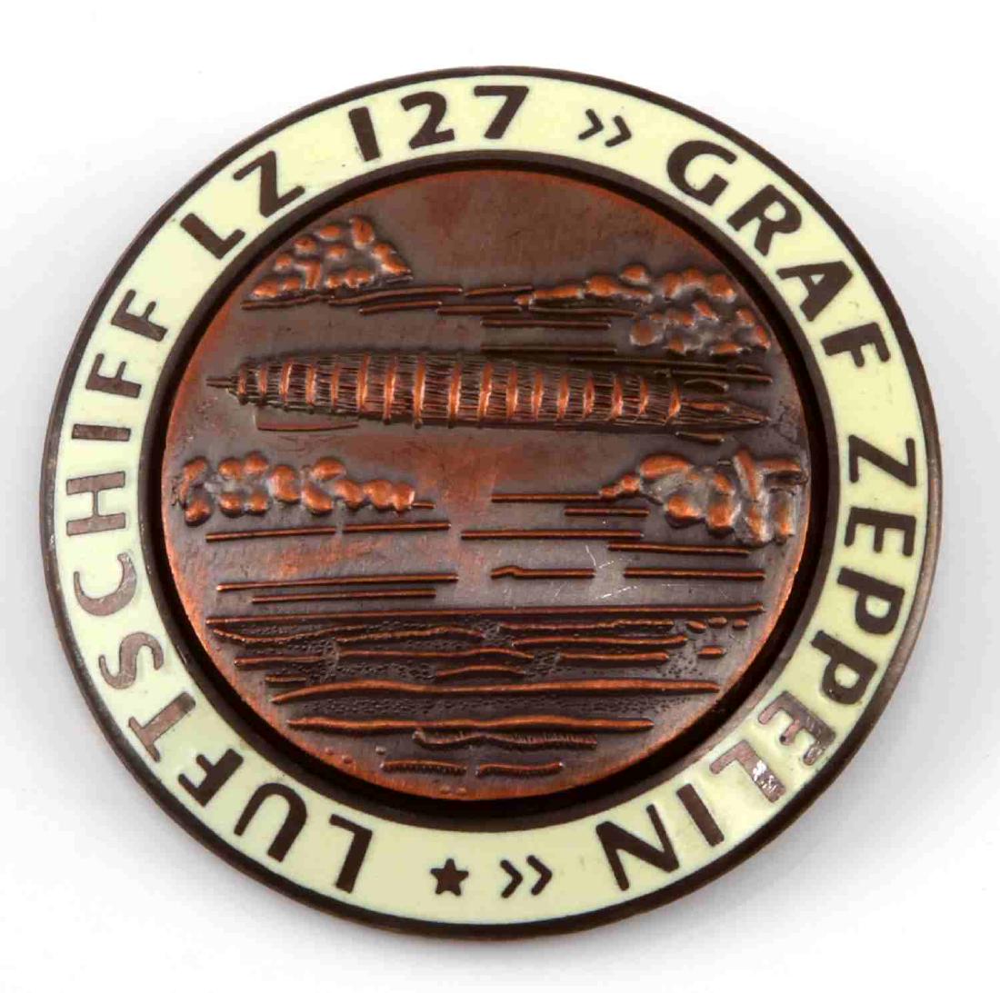 GERMAN WWII GRAF ZEPPELIN LZ 127 AIR SHIP BADGE: 1 3/4 inch diameter. Reverse maker marked "FLL". Thin horizontal pin back. Two-piece copper and beige enamel construction. Unauthenticated. Sold "as is".