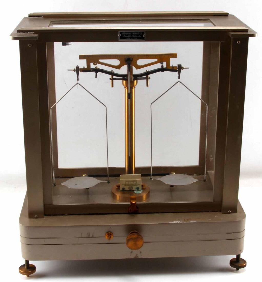 VINTAGE ARTHUR H THOMAS BRASS BALANCE SCALE: Brass balance scale in an aluminum and glass case. Measures 10x16.5x17.5 inches. In very good condition, with minor surface scuffing. One of the controls on the front of the scale is missing its screw
