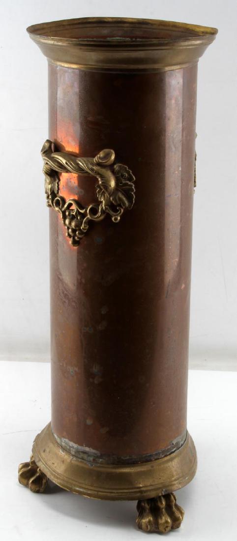 ANTIQUE COPPER WITH BRASS ACCENTS UMBRELLA STAND: Straight copper body atop brass claw foot stand. It has brass handles with grape vine motif. Brass trim has several indentations and is missing rim cap. Height 25 inches with a 9.5 inch diameter.