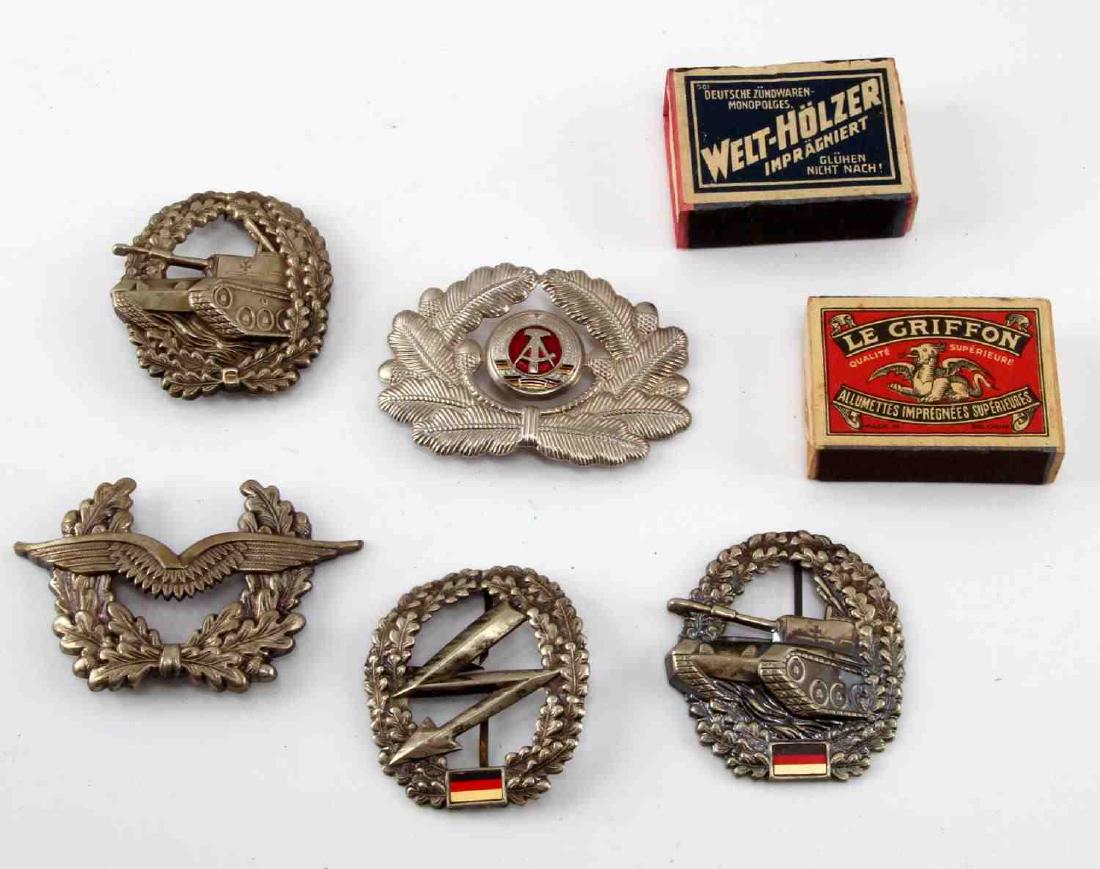 5 GERMAN COLD WAR ERA BERET & CAP BADGES: West German items include 2 tank badges, army signal badge, and air force cap badge. East German items include a border guard visor cap badge. Also included with lot are 2 WWII era match boxes from Be