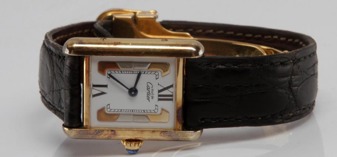 MUST DE CARTIER VERMEIL TANK QUARTZ WATCH SWISS: Gold tone rectangular shape with Roman numerals at 12 and 6, gold tone pieces accent the face of the watch with 'Must De Cartier' at top. Blue crown. Back of case is maker marked with serial numbers a