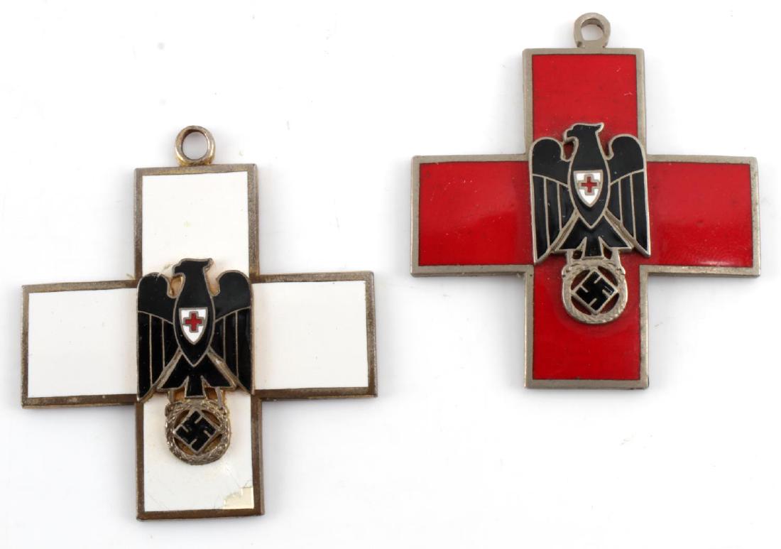 WWII GERMAN THIRD REICH RED CROSS MEDAL LOT OF 2: Two WWII German Red Cross medals. One has red enamel and the other has white enamel. The white enamel one has minor damage on the bottom section. Both have maker marks on the back.