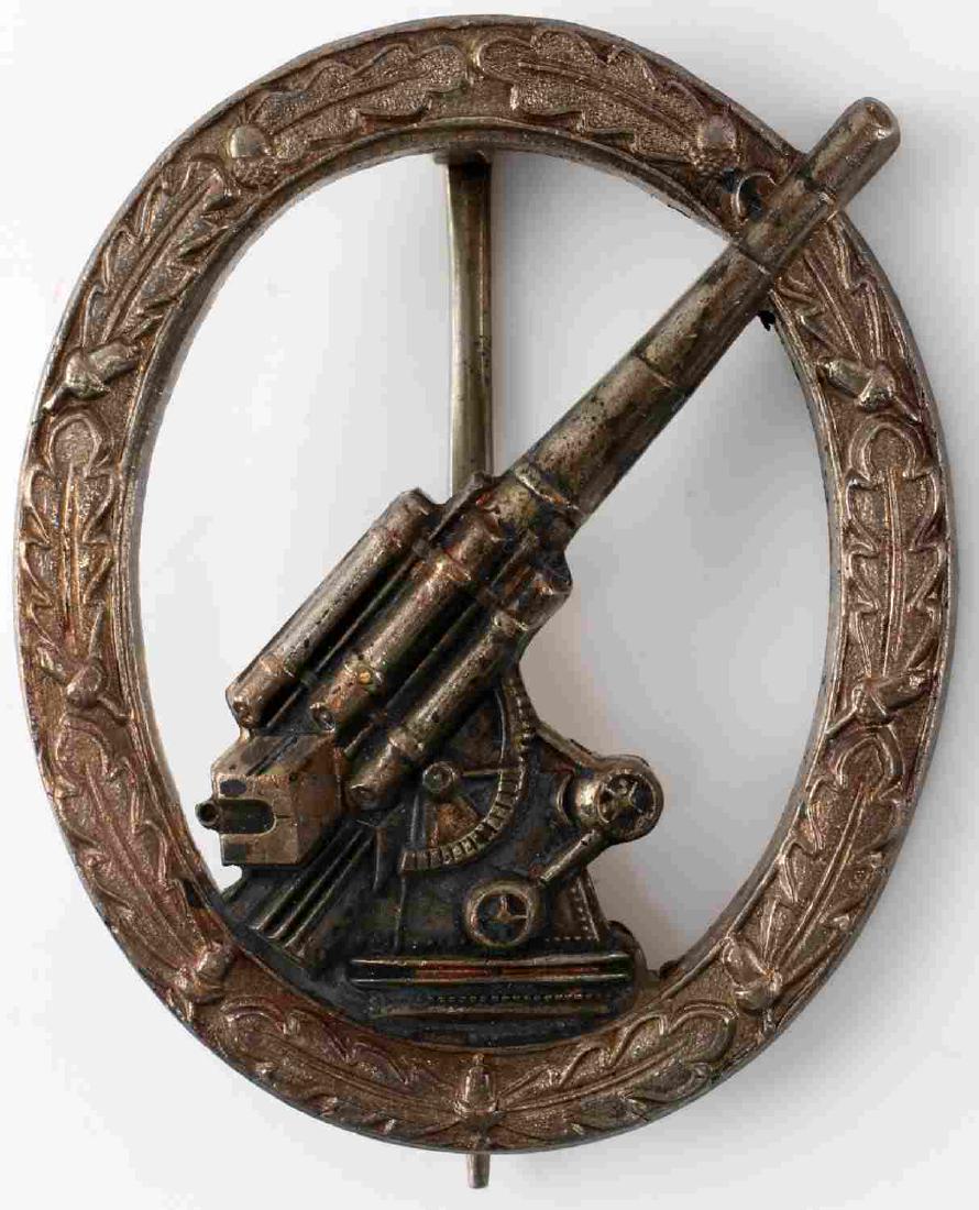 GERMAN THIRD REICH WWII ARMY FLAK ARTILLERY BADGE: West German WWII 1957 army silver flak artillery badge. The front shows a flak 88 gun in the center surrounded by an oval oak leaf wreath. Has a wide vertical pin back. One piece nickel construction.