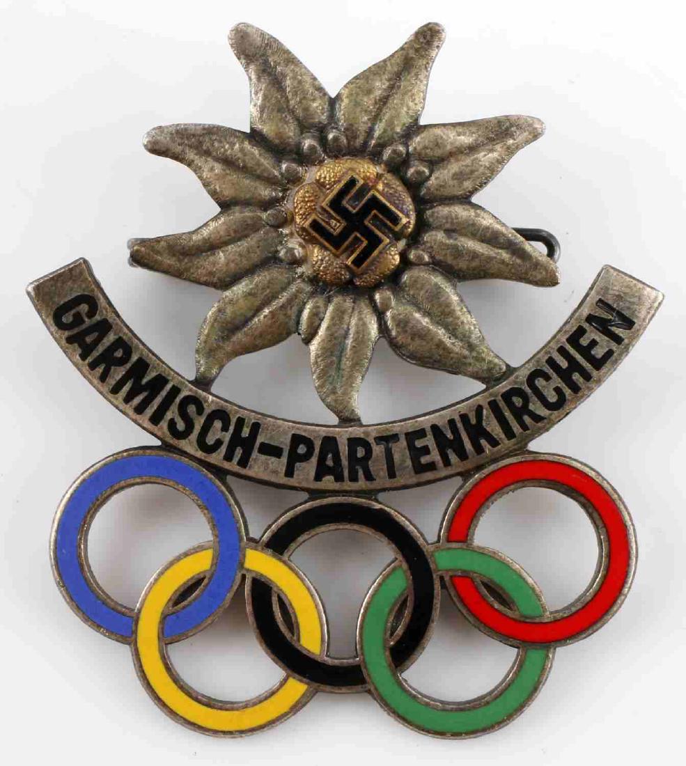 WWII WINTER OLYMPICS BADGE GARMISCH PARTENKIRCHEN: German World War II 1936 Winter Olympics Badge with edelweiss flower and the Olympic rings. The front reads "Garmisc-Partenkirchen", the reverse is marked ‘Annestsberger Munchen’ around the pin. M