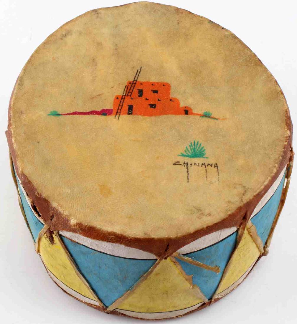 NATIVE AMERICAN SIGNED STRETCHED RAWHIDE DRUM: Decorated Native American stretched rawhide drum. Painted and signed "Chinana" on top. Good condition overall with some repairs, staining, and signs of abrasions present. 6.5" in diameter and stands 4