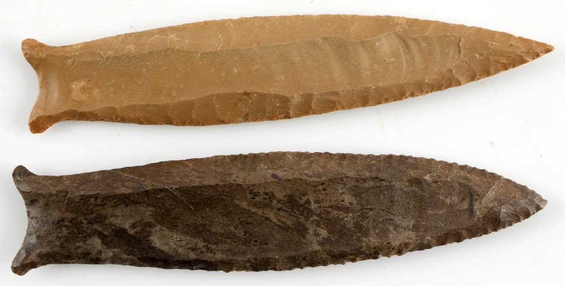 2 LATE PALEO CUMBERLAND ARROWHEAD POINTS: One made of dark grey brown chert with darker inclusions, flared ears, double flute, excellent parallel flaking. One creamy beige chert with parallel flaking, flute to each side, and flared ears. Meas