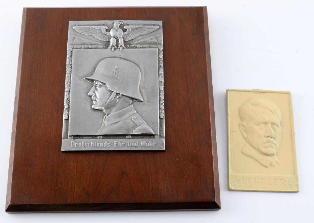 2 WWII THIRD REICH PLAQUES ARMY AND ADOLF HITLER: One aluminum plaque on wood of a German soldier profile with 'Deutschlands Ehr und Wehr' at the bottom, entire piece measures 10.5 X 10 inches. The other piece is a painted iron hanging piece with Hit