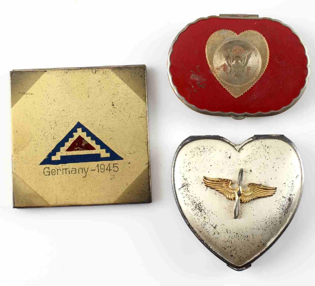 WWII MILITARY MAKEUP COMPACT SWEATHEART LOT OF 3: WWII US sweetheart makeup compacts including 1 with heart shaped compact with Air Force wing badge, 1 with 7th Army "Germany-1945," and 1 with US army eagle inside a heart. Compacts show wear and sign