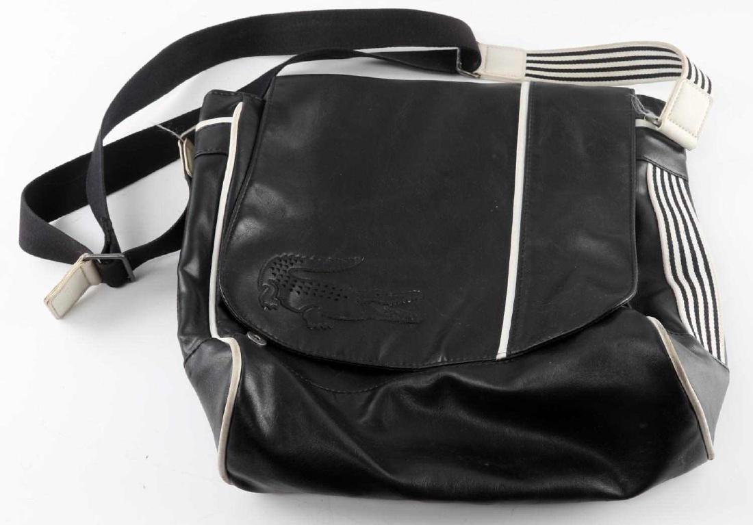 BLACK LACOSTE SHOULDER BAG W WHITE LINING: Lacoste emblem on front of bag. Single strap is black and white striped. PVC exterior and polyester interior. Bag has slight scuff marks on bottom and has slight discoloration in areas. Measures 9.25