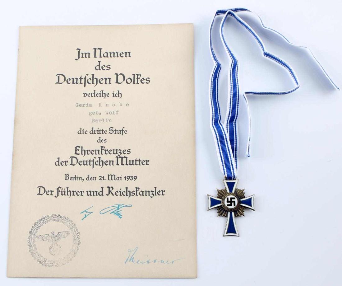 WWII GERMAN MOTHERS CROSS AND CITATION LOT: German Mother's Cross medal in bronze with citation. Citation facsimile signed by Adolf Hitler and Otto Meissner. Named to Gerda Knabe. Excellent condition overall. Unauthenticated; sold as is. This l
