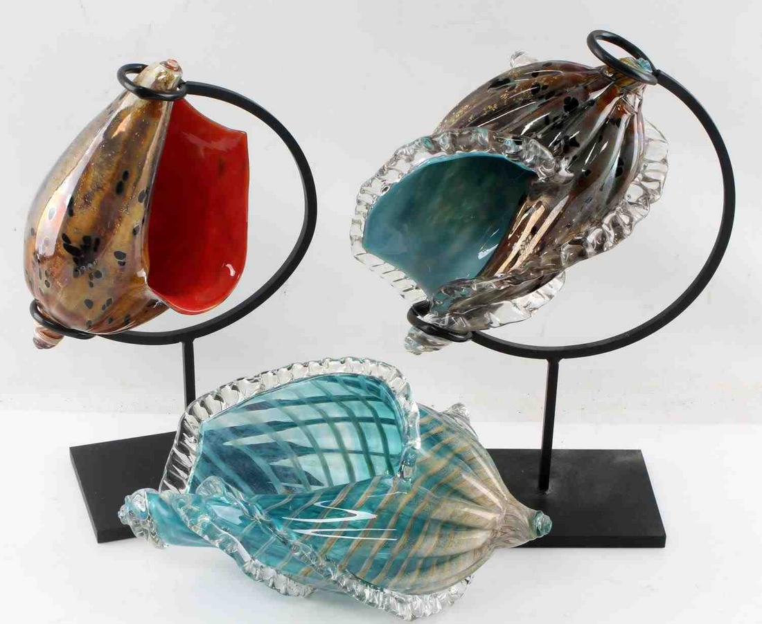 3 CHARLES FRIEDMAN CONCH SHELL ART GLASS PIECES: One burnt orange and metallic conch shell. Measures 8.5 inches. On stand. Has certificate of authenticity and is signed. One blue and metallic conch shell. Measures 10.5 inches. On stand. Has certific