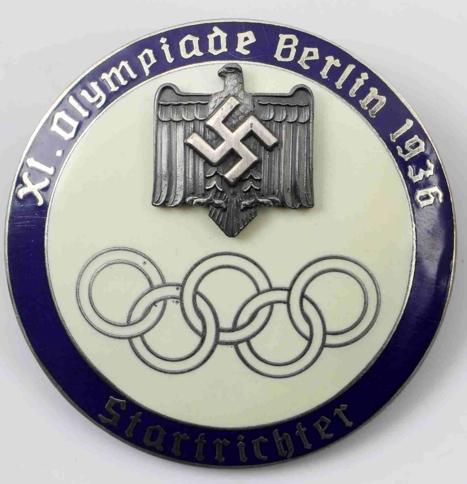 WWII GERMAN THIRD REICH BERLIN OLYMPIC GAMES BADGE: German 1936 Olympics Berlin 1936 Startrichter badge. Reverse marked "Ges Gesch PJC." Two piece nickel construction with blue and beige enamel. Has thin horizontal safety pin back. Excellent condition.