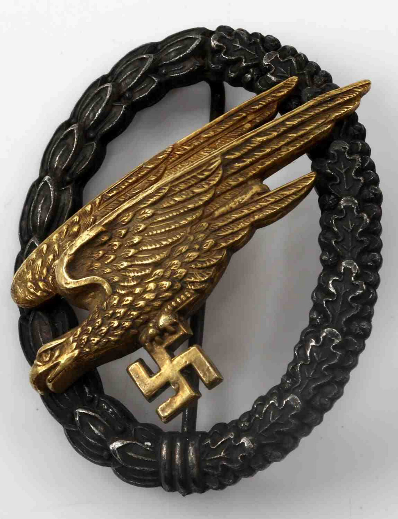 WWII GERMAN FALLSCHIRMJAGER PARATROOPER BADGE: German Fallschirmjager badge. 2-piece domed rivet construction with thin vertical pin back. Reverse maker marked "C.E. Juncker Berlin S.W." Very good condition overall. Unauthenticated; sold as is.