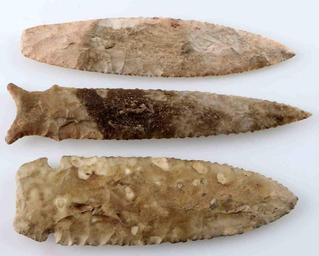 LOT OF THREE EARLY ARCHAIC STYLE ARROWHEAD POINTS: Graham Cave style point out of multi-tone brown lithic, parallel flaking, finely serrated edge sharp to touch. Measures 6 inches. Nebo Hill style point of creamy pink and white lithic, random flaking 