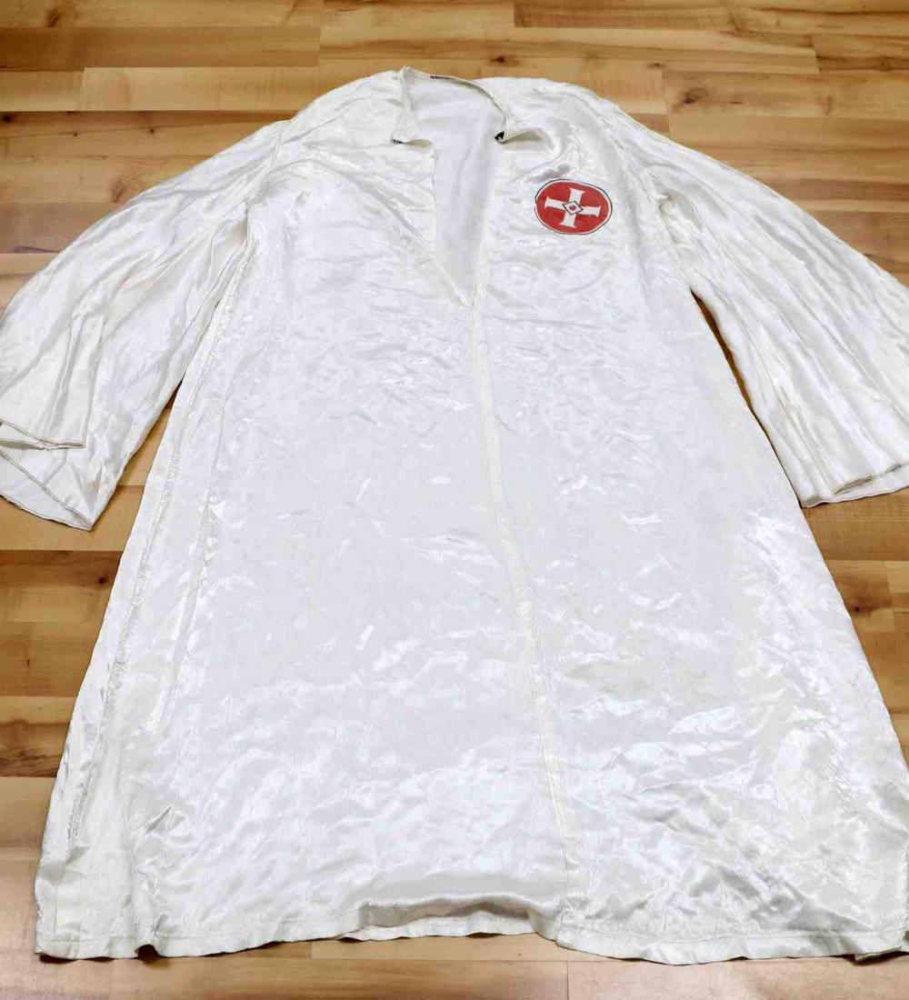 KKK 2ND KU KLUX KLAN 1920S KLAN ROBE: 2nd generation 1920s-1930s KKK robe. Satin construction with affixed red tear drop patch. Robe has 1 bakelite snap closure at its top and inked with a name (and then crossed out) at its collar. In goo