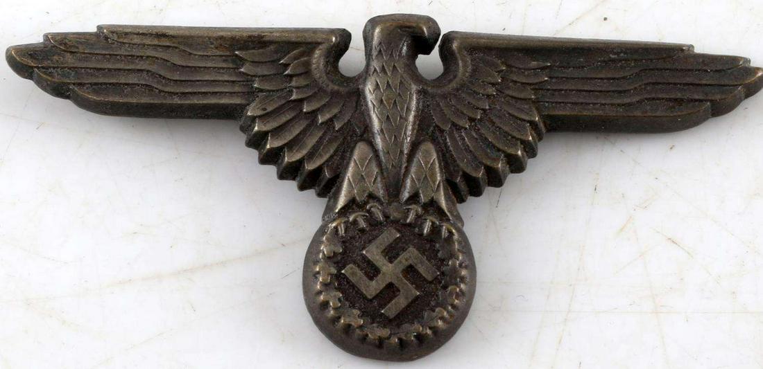 WWII GERMAN SS SCHUTZ STAFFEL VISOR CAP EAGLE: Measures 2 3/4” wide by 1 1/4” tall. The reverse side is maker marked ‘RZM M1/34’. Has three flat prongs on the reverse side for attaching to the visor cap. Stamped nickel construction. In ver