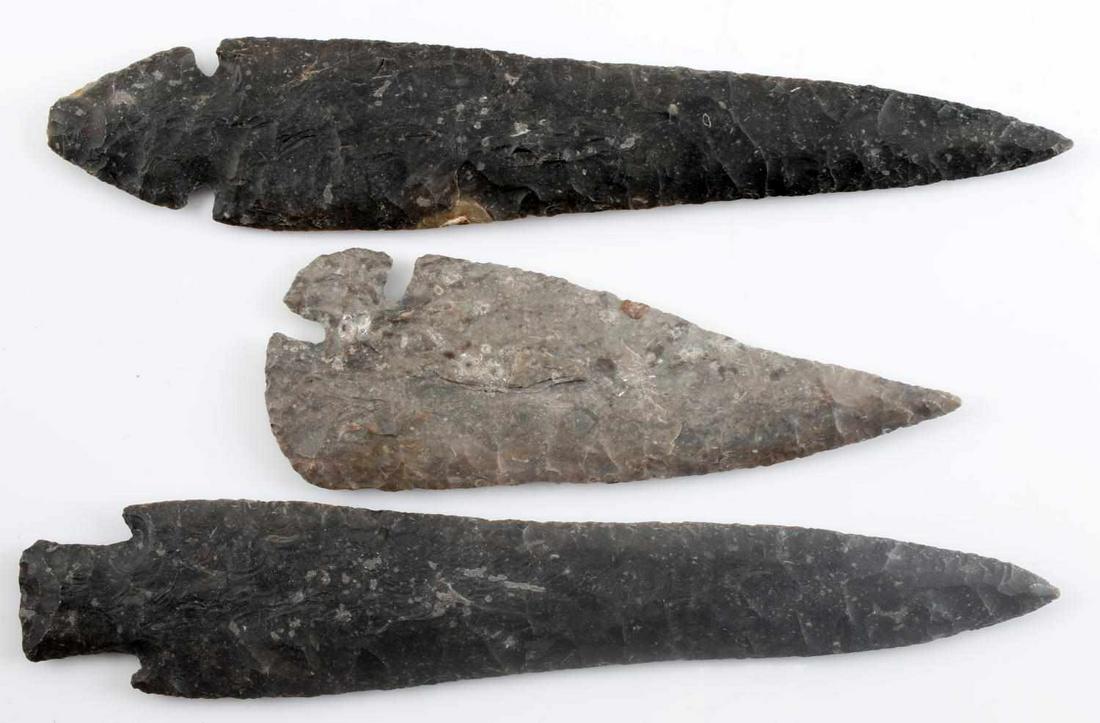 LOT OF THREE NATIVE AMERICAN ARROWHEADS: Three very finely carved arrowheads of dark gray lithic. One waisted Benton point with narrow random flaking. Measures 8.5 inches. One tang with narrow, largely random flaking. Measures 6 inches. One 