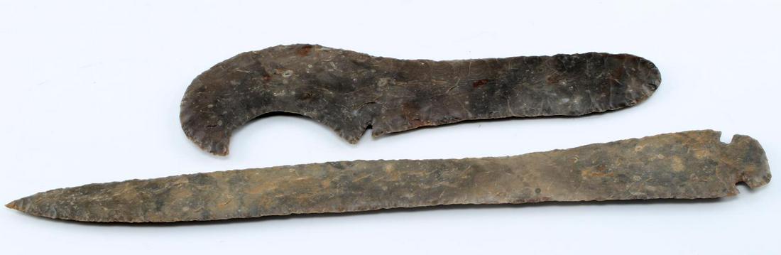 LOT OF TWO NATIVE AMERICAN ARROWHEADS ECCENTRIC: One eccentric point of dark brown lithic in sickle-like shape with small notch. Narrow to broad nice flaking. Measures 11 inches. Small area of glue residue on back from where the piece was affixed. O