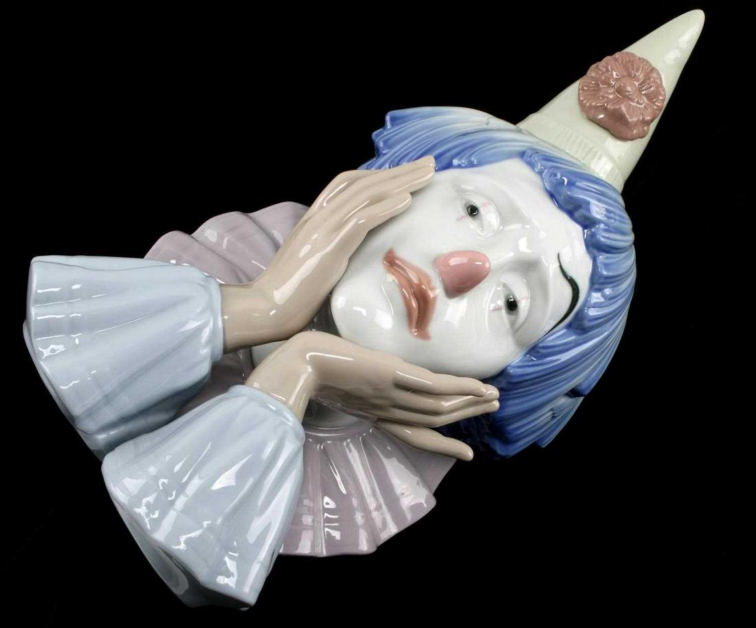 ORIGINAL LLADRO CLOWN HEAD MADE IN SPAIN 5129: Clown's head, designed by Jose Puche, from the year 1982, measuring 13 inches by 6.25 inches in near new condition. The clown has blue-colored hair and is wearing an ivory cone hat with a red flower. 