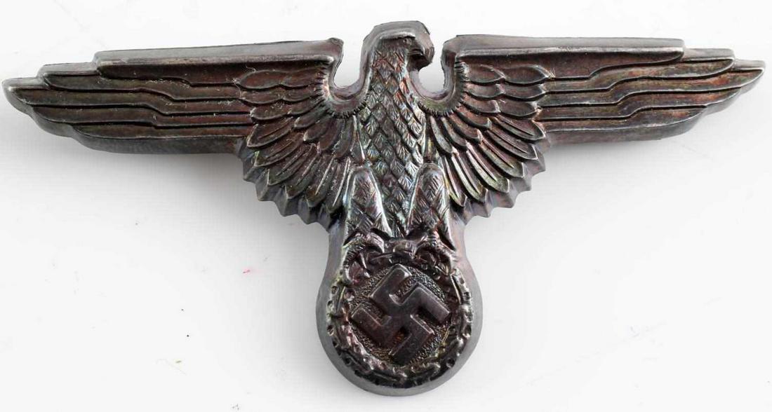 GERMAN WWII WAFFEN SS OFFICERS VISOR CAP BADGE: German WWII Waffen SS Officers Visor Cap Eagle. The reverse side is maker marked ‘RZM M1/52’. Measures 2.75 inches across. Has two flat horizontal prongs on the reverse side. Stamped nickel constr