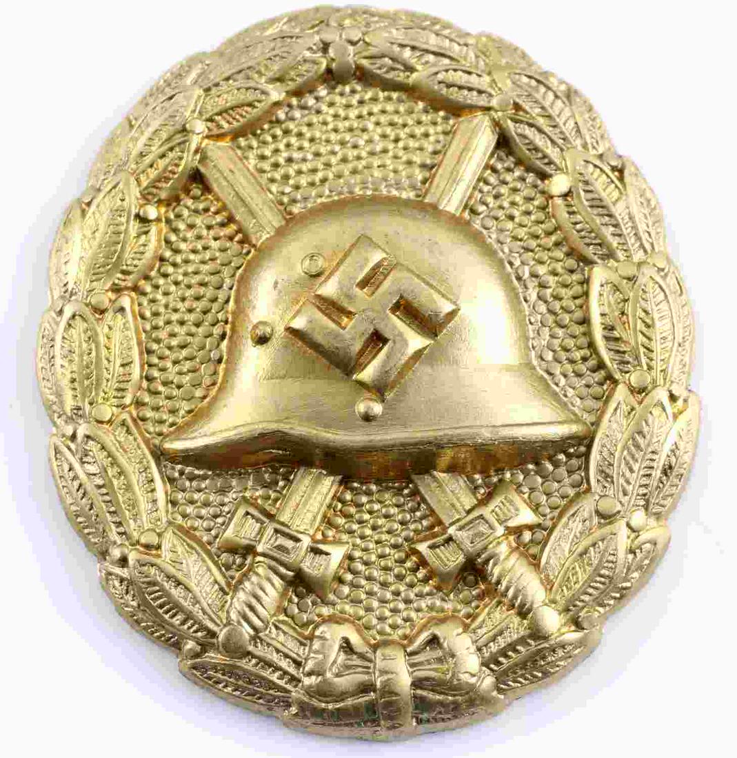 WWII GERMAN GOLD SPANISH CONDOR LEGION WOUND BADGE: German WWII Gold Spanish Condor Legion Wound Badge. The front shows a German helmet in the center with a pair of crossed swords in the back ground. All three are surrounded by an oval oak leaf wreath.