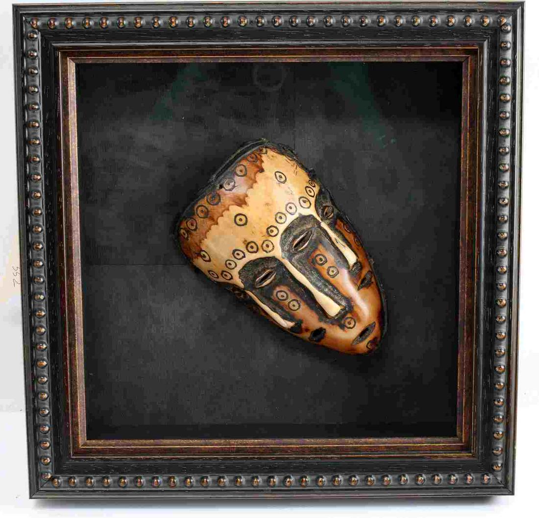 VINTAGE HAND CARVED AFRICAN BONE MASK IN FRAME: Features lentoid eyes and mouth, long noses and other circular design. Measures 5.5 X 3.5 inches. Shadow box frame measures 12 X 12 X 3 inches. Very good condition.