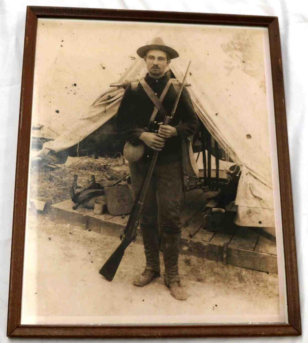 FRAMED SPANISH AMERICAN WAR PRINT PHOTO: Framed reprint of a photograph of a soldier dressed in uniform holding rifle with bayonet. Dimensions including wood frame measure 14.75 by 11.75 inches. Has cardboard backing with brass hangers.