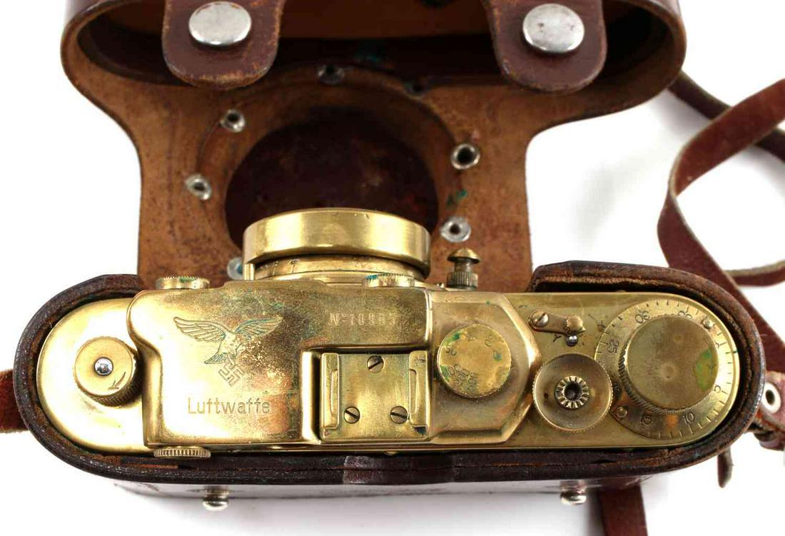 WWII THIRD REICH LUFTWAFFE LEICA CAMERA & CASE: One brass and leatherette shell Luftwaffe Leica camera in brown leather case with 18 inch straps. Camera measures 6 inches by 3 inches by 1 inch and has eagle and Swastika symbol on lens cover. The ea