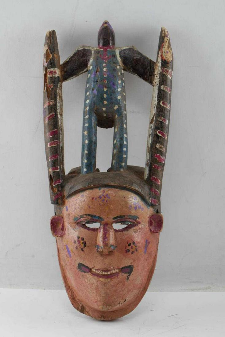 LOT OF TWO IBIBIO NIGERIA POLYCHROME WOOD MASK: One wood painted mask with bird with outstretched wings holding onto snakes. Measures 18.5 inches by 3.5 inches by 7.5 inches. Some damage to wood in areas. One wood painted mask showing soccer player