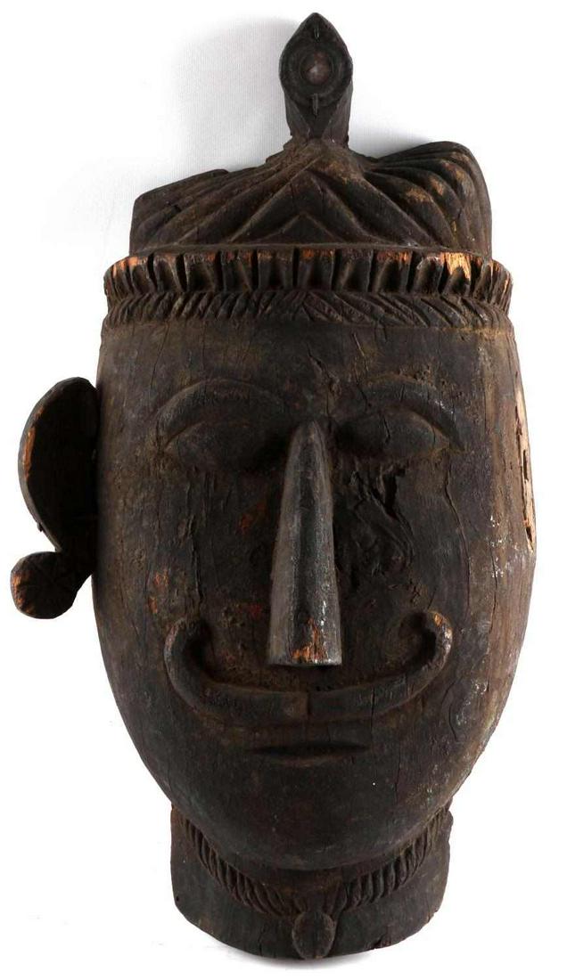 NEPAL FESTIVE WOOD ETHNOGRAPHIC HEAD WITH MIRROR: Nepal Wooden Carved Head with Mirror. The head weights 14.6 pounds. Measures approximately 30 by 15 inches. The left ear is missing, there is a small mirror at the top of the hat but, it is cracked. T
