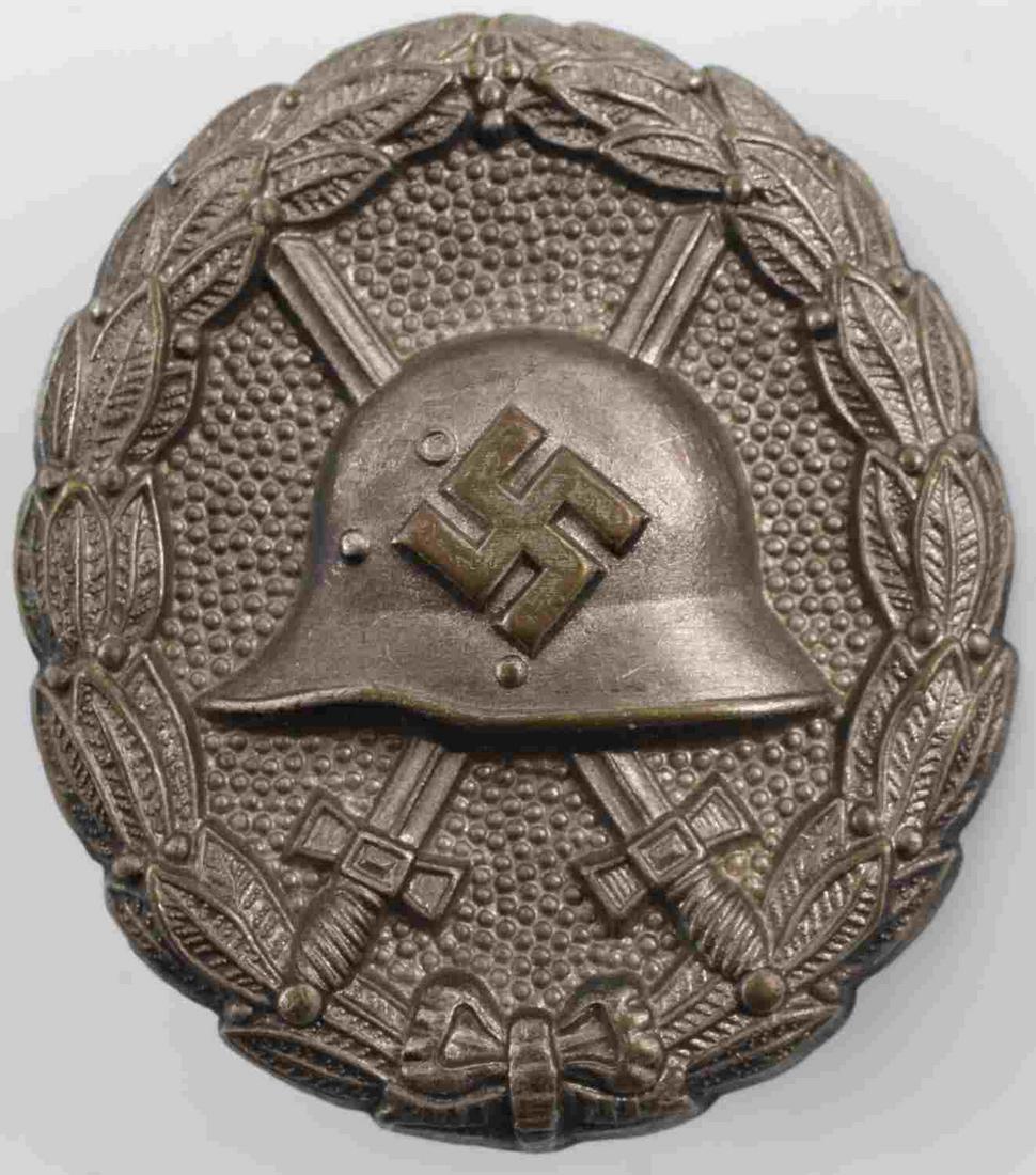 GERMAN WWII CONDOR LEGION WOUND BADGE: German WWII Silver Condor Legion Wound Badge. The front shows a German helmet in the center with a pair of crossed swords in the back ground. All three are surrounded by an oval oak leaf wreath. Has a