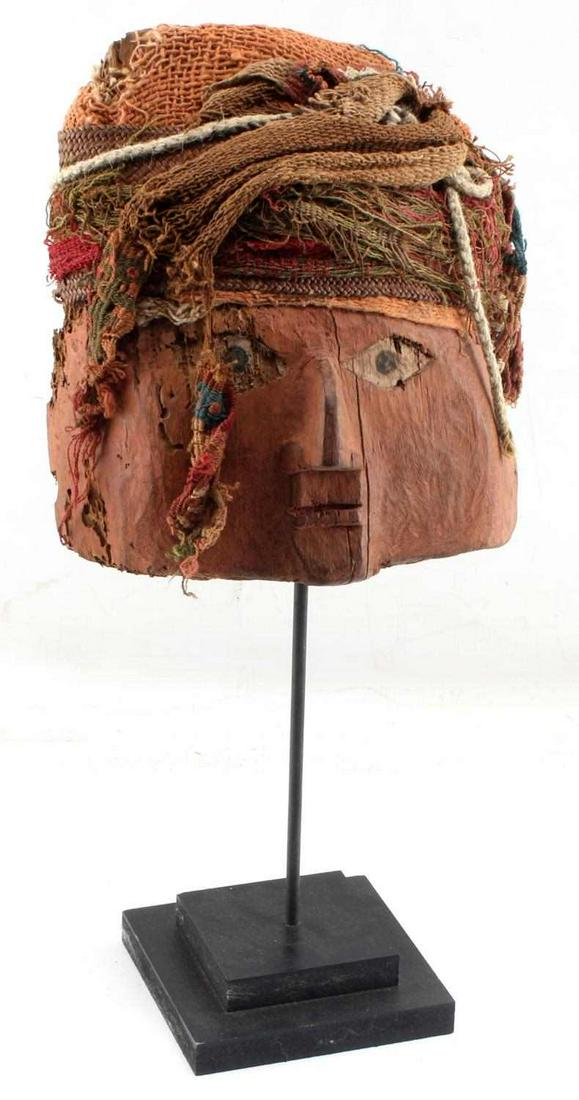 CHANCAY WOOD MUMMY MASK W TEXTILE HEAD WRAP: Pre-Columbian. Some chips to eyes. Measures 9.5 inches (17 inches w stand) by 8 inches. Provenance: Previously sold Skinner Auctions 5/15/10.