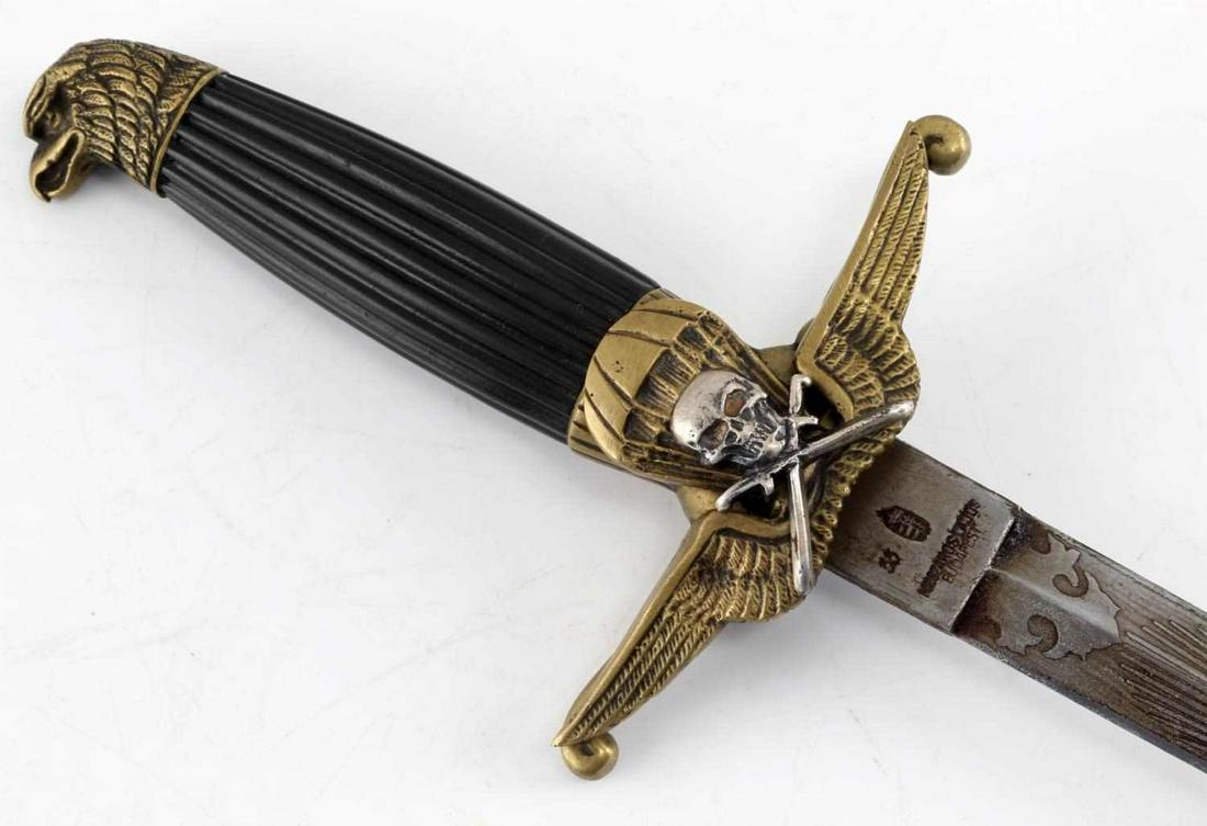 WWII HUNGARIAN PARATROOPER DAGGER WITH SCABBARD: Engraved brass fittings and design with eagle's head pommel, hard black plastic grip, skull with crossed swords affixed to front of crossguard, sharp triangular blade measures 8.25 inches long with pa