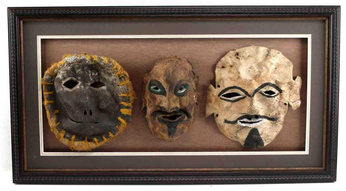 LOT OF 3 ETHNIC HIDE LEATHER MASKS IN OPEN FRAME: Maybe early Mexican, all three seem to be made from animal hide and painted, the left one with added fabric. Measure 9 - 10.5 inches long. In open frame that measures 33 X 18 inches. Hanger to back. V