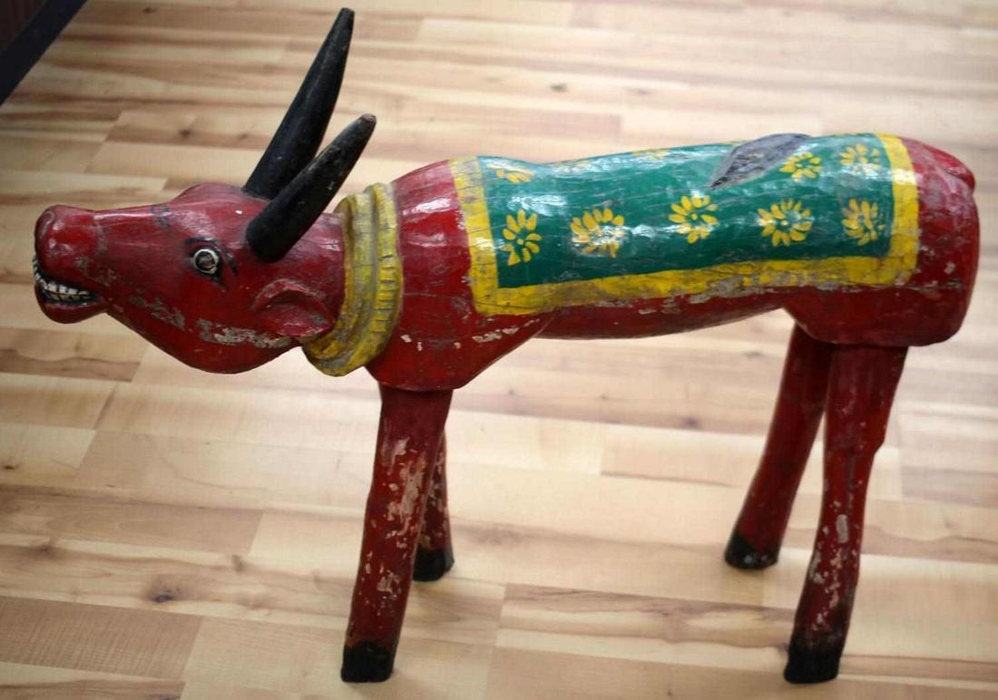 ANTIQUE WOOD POLYCHROME INDIA SACRED COW STATUE: Hand carved from solid piece of wood, polychromed antique temple statue of India's sacred cow. In good condition with some loss of paint and aged patina. Dimensions are 26x34x8 inches This lot has a r
