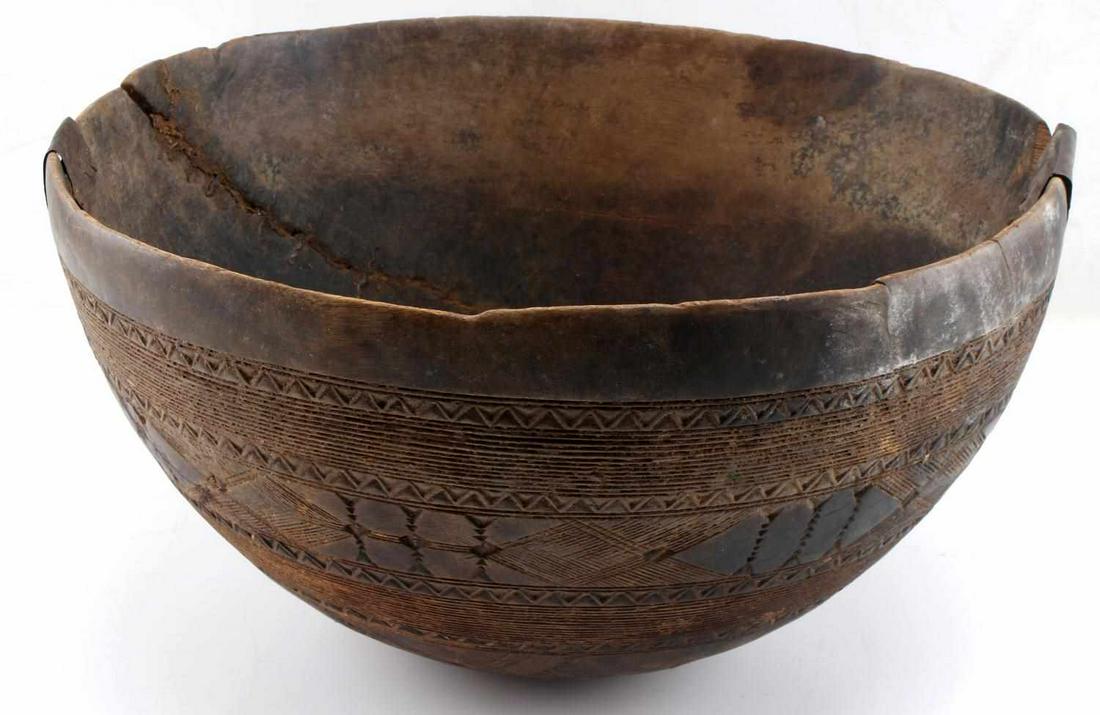 OLD AFRICAN CARVED WOOD BOWL: Antique African wood bowl, height 8 inches diameter 14 inches, featuring incised geometric pattern, remnants of clay coating and metal tacked repairs to rim. Bowl has considerable use wear. This lot h