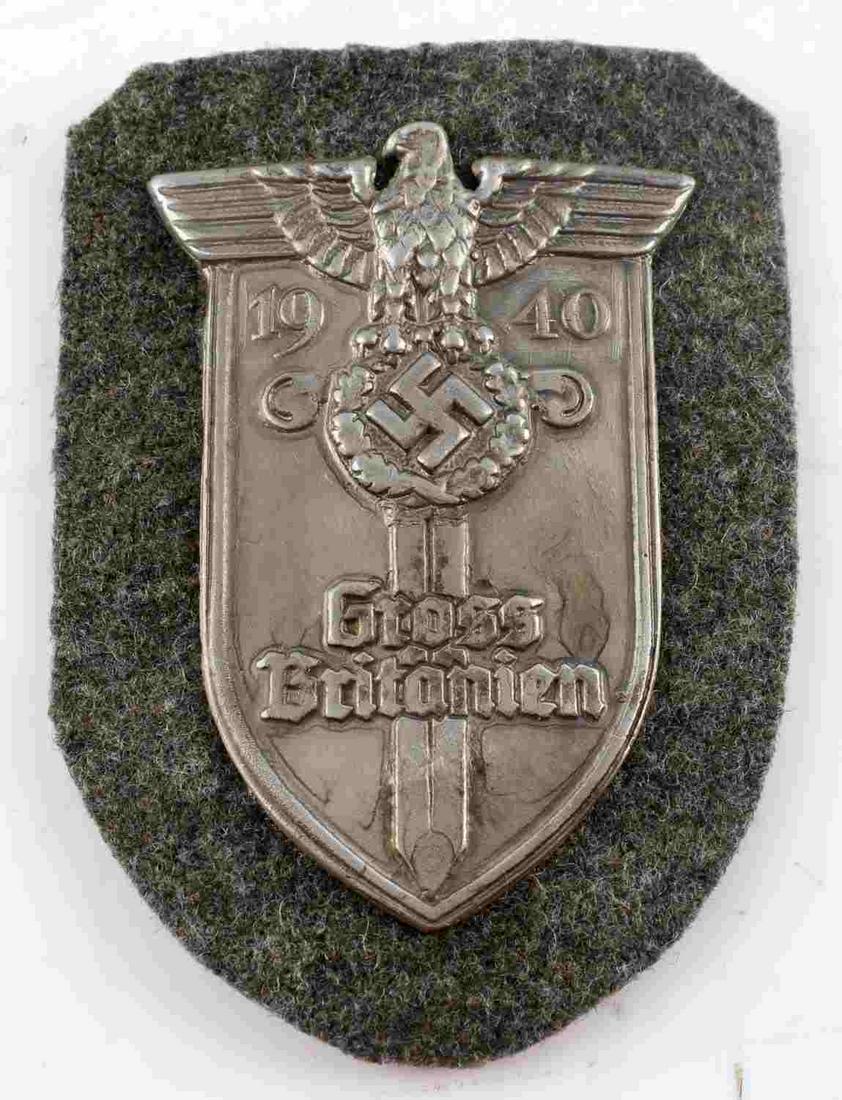 WWII GERMAN THIRD REICH GROSS BRITANIEN SHIELD: WWII German Third Reich Gross Britanien Shield. "FAD" printed on the rear. Green wool placed on brown paper. Measures 3 by 2.25 inches. Dated to 1940. Some finish loss is present. Overall, very good c