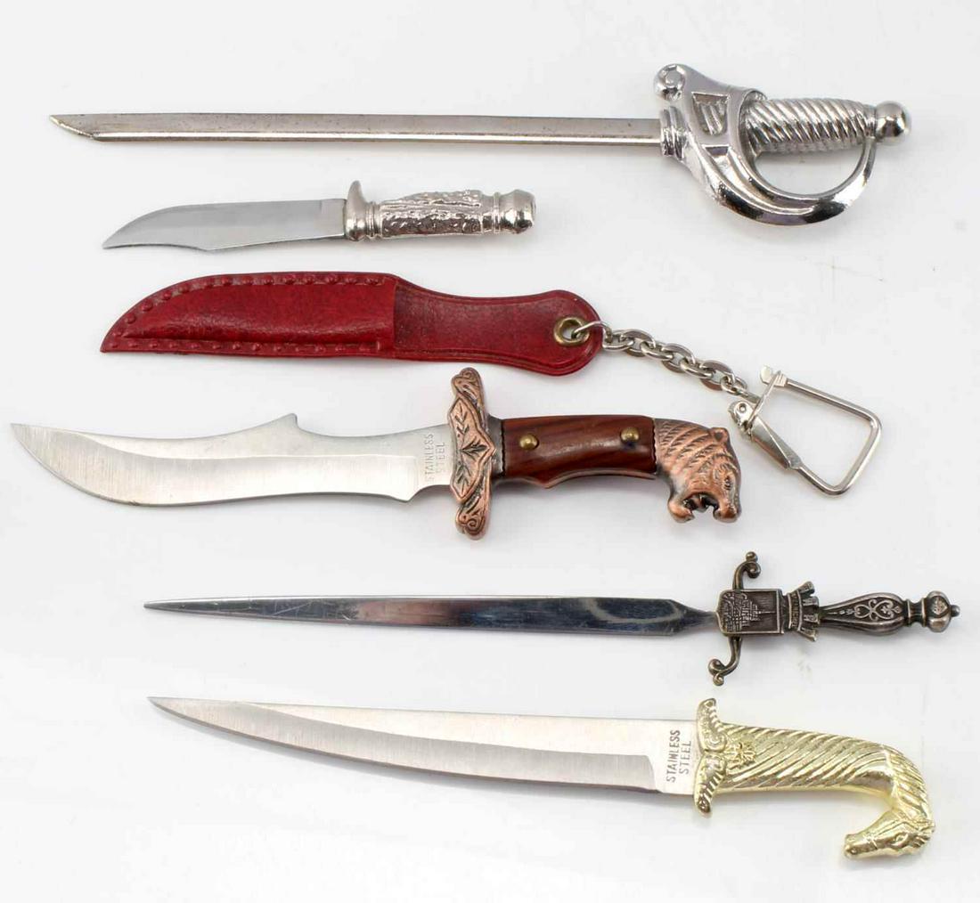 LOT OF 5 MINIATURE KNIVES AND SWORDS ONE SCABBARD: Lot of five miniature swords and knives, one with keychain scabbard. Measure 6 inches on average with a 4 inch blade. Two have a sharp edge. Overall, good condition.