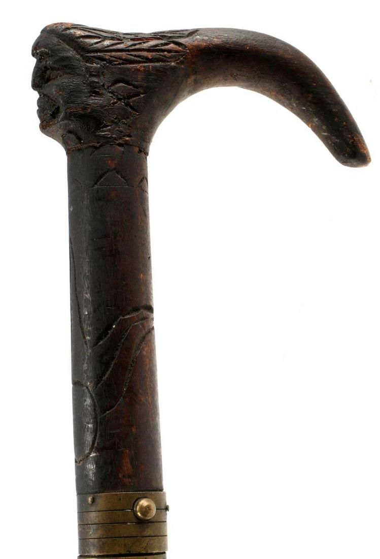 ANTIQUE WOOD CARVED INDIAN HEAD SWORD WALKING CANE: Beautifully Carved Indian Head Grip Sword Cane/Walker. No maker's markings visible. Original Ferrule. Measures 26.25 inches from the grip to the tip of the blade and 37 inches in its entirety. Wood sc