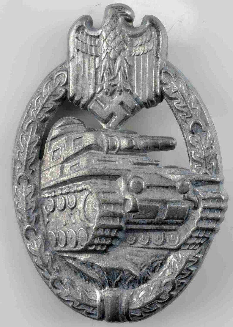 GERMAN WWII ARMY SILVER TANK ASSAULT BADGE: The front shows a tank in the center with a German eagle clutching a swastika in his talons at the top. Both are surrounded by an oval oak leaf wreath. Has a thin vertical pin back with a ‘c’ catc