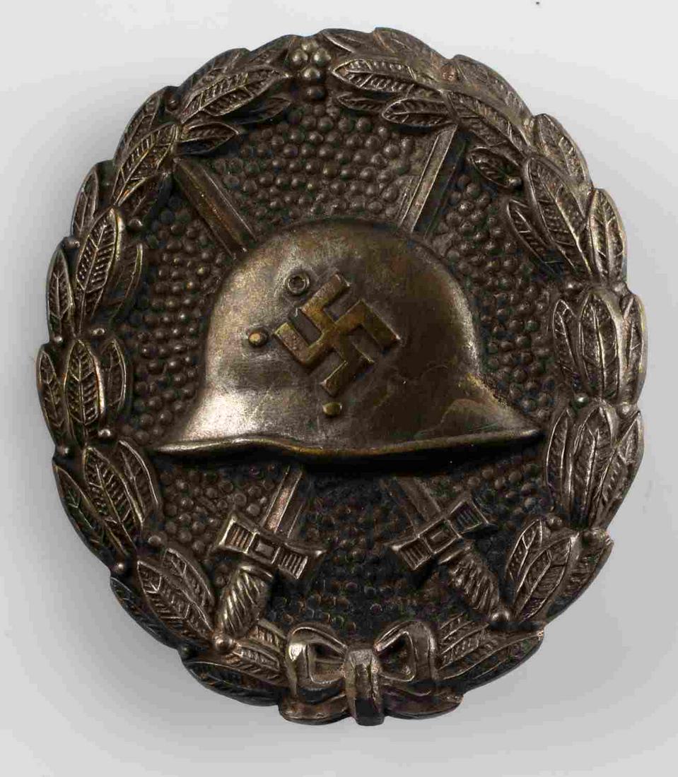 WWII GERMAN SILVER SPANISH CONDOR LEGION BADGE: WWII German Silver Spanish Condor Legion Wound Badge. The front shows a German helmet in the center with a pair of crossed swords in the back ground. All three are surrounded by an oval oak leaf wreat