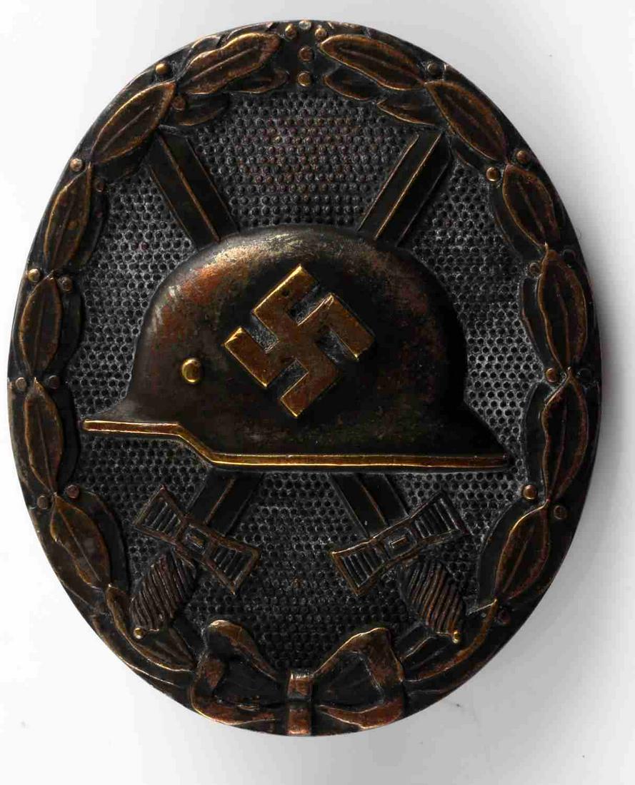 WWII GERMAN THIRD REICH GOLD WOUND BADGE: WWII German Gold Wound Badge. The front shows a German helmet in the center with a pair of crossed swords in the back ground. All three are surrounded by an oval oak leaf wreath. The reverse side is m