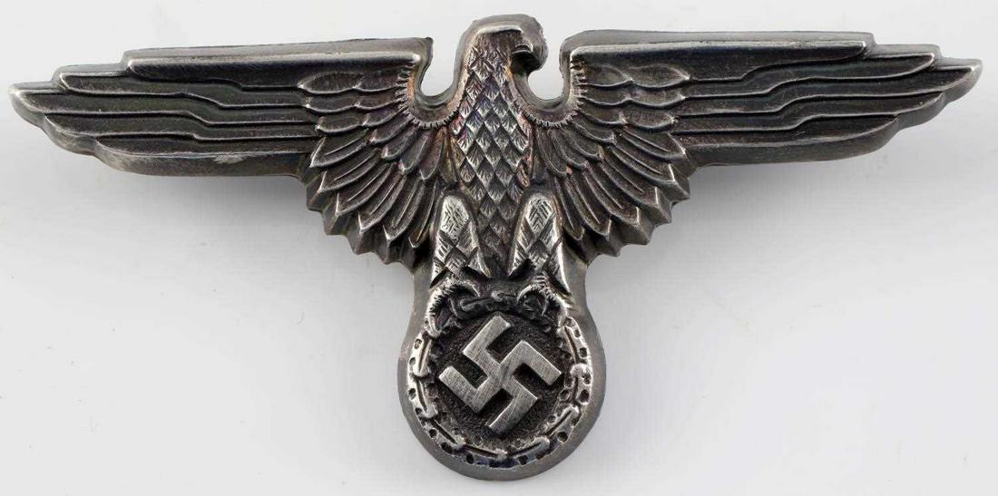 GERMAN WWII WAFFEN SS OFFICERS VISOR CAP EAGLE: Measures 2 3/4" wide by 1 5/16” tall. The front shows a Waffen SS eagle clutching a swastika in his talons. The reverse side is maker marked ‘RZM M1/14’. Has two flat horizontal prongs crimped i