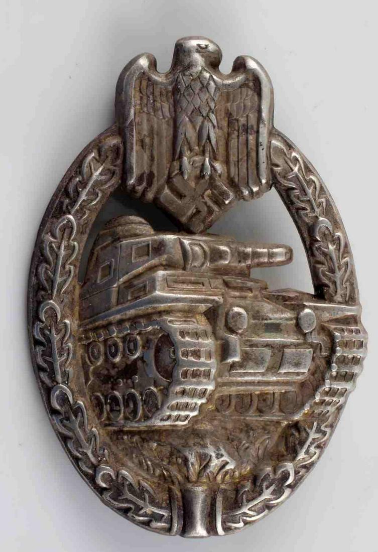 GERMAN WWII ARMY SILVER TANK ASSAULT BADGE: The front shows a tank in the center with a German eagle clutching a swastika in his talons at the top. Both are surrounded by an oval oak leaf wreath. Has a thin vertical pin back with a ‘c’ catc