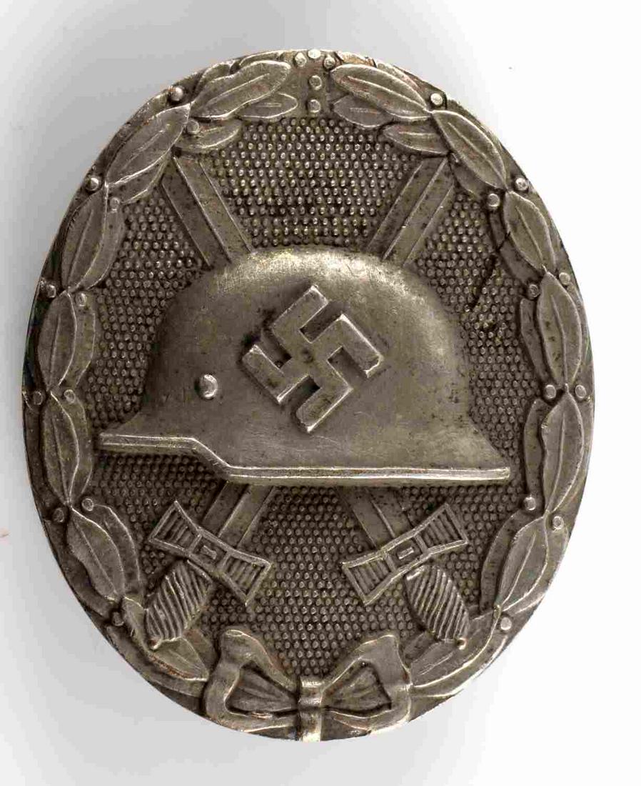 WWII GERMAN THIRD REICH SILVER WOUND BADGE: WWII German Silver Wound Badge. The front shows a German helmet in the center with a pair of crossed swords in the back ground. All three are surrounded by an oval oak leaf wreath. The reverse side is