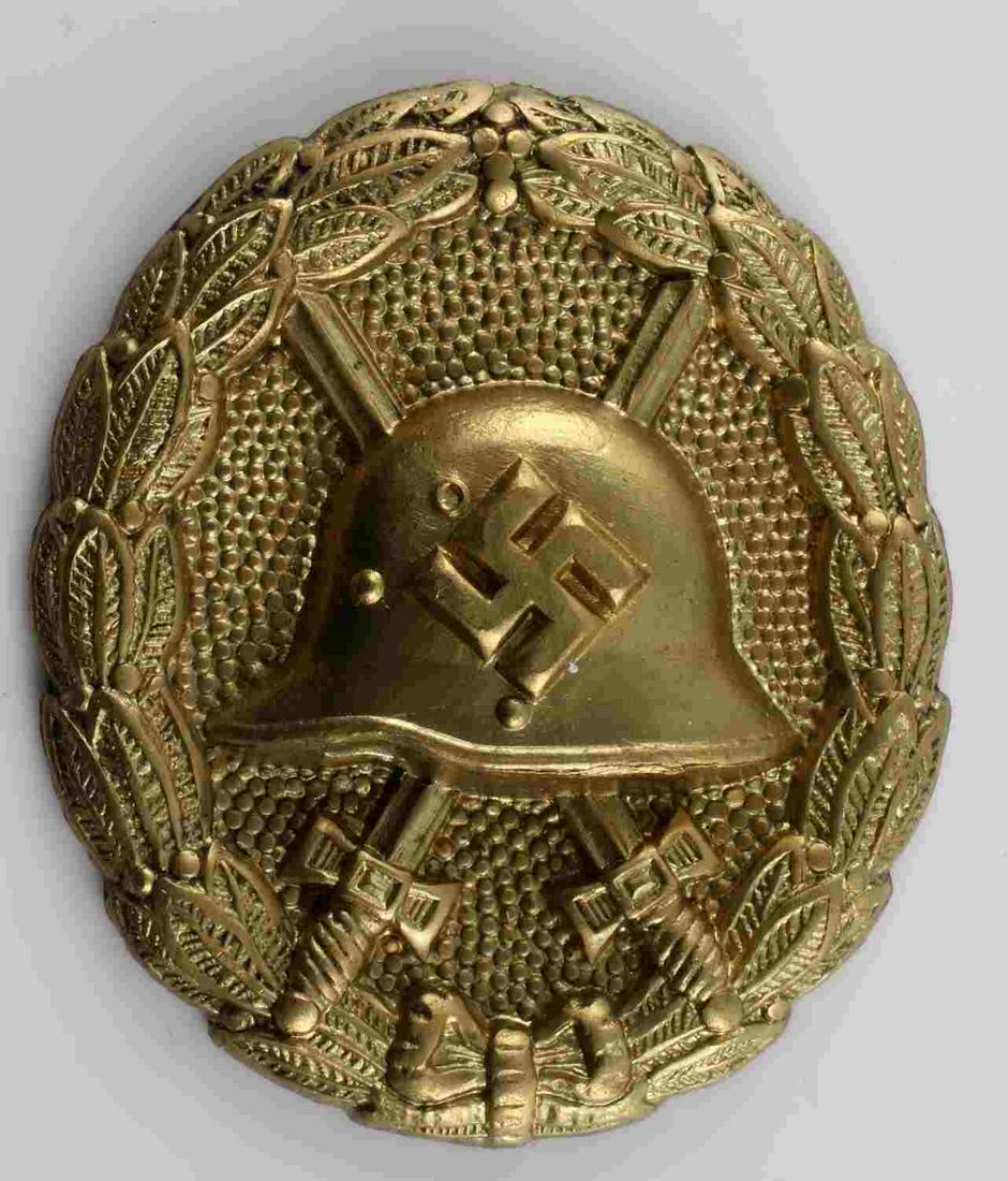 GERMAN WORLD WAR II GOLD CONDOR LEGION WOUND BADGE: The front shows a German helmet in the center with a pair of crossed swords in the back ground. All three are surrounded by an oval oak leaf wreath. The pin and catch are not present. Stamped brass co