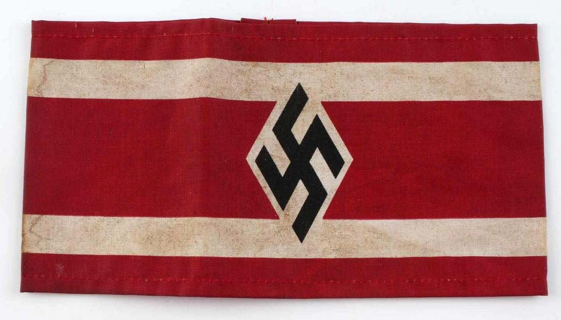 GERMAN WWII STUDENTBUND SWASTIKA ARM BAND: Measures 7 7/8” wide by 4 1/8” tall. The front shows a swastika in a diamond in the center of a red back ground with two white stripes. One piece machine sewn printed cotton construction. This was