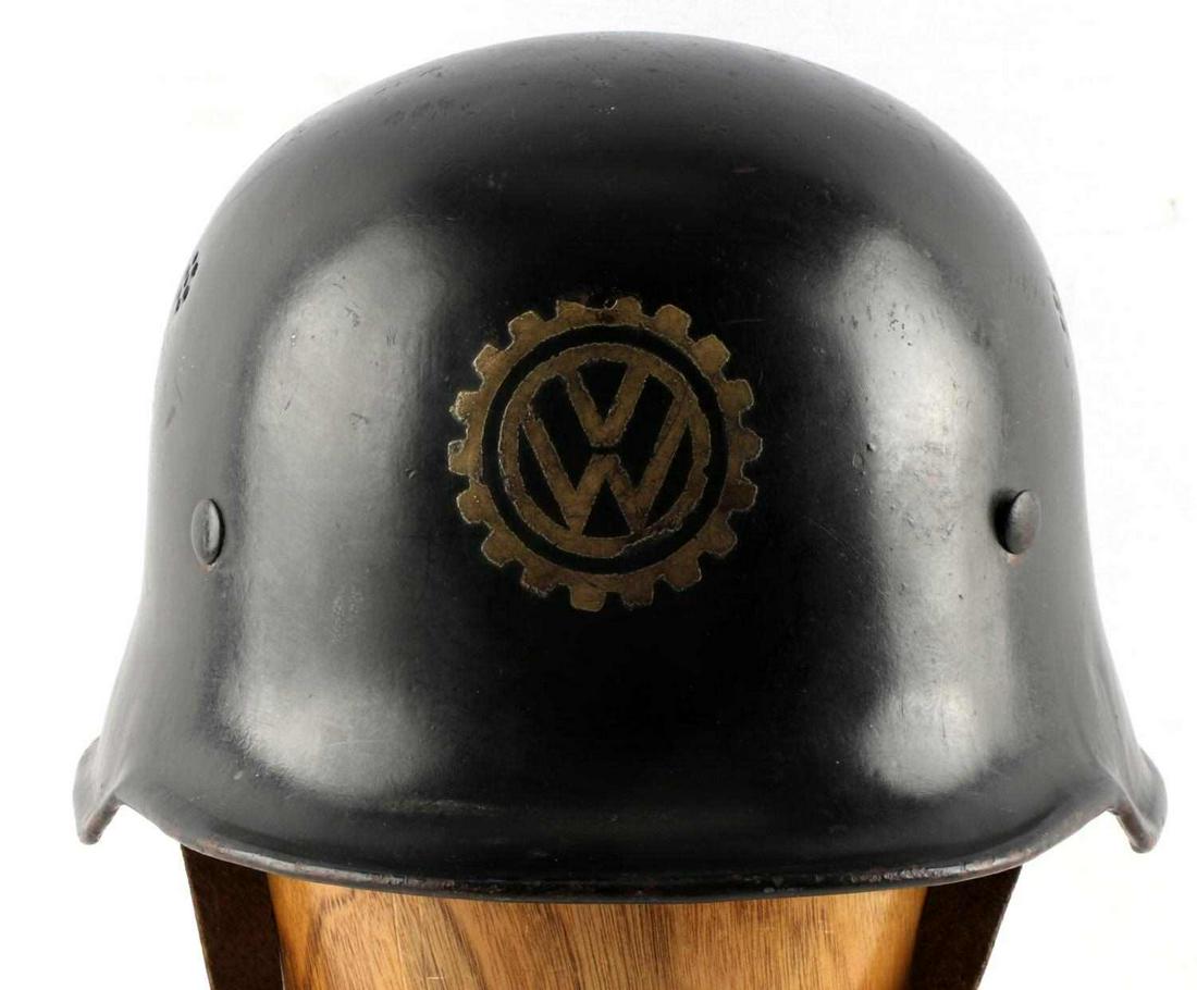 WWII GERMAN VOLKSWAGEN FACTORY WORKER HELMET: German Third Reich era Volkswagen factory workers M40 helmet with 9-finger liner and chin strap. Volkswagen logo surrounded by gear on front of the helmet likely added post-war. Liner stamped with the
