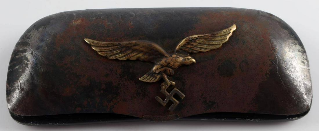 GERMAN WWII REICH LUFTWAFFE PILOT GLASSES CASE: German Third Reich Luftwaffe pilot's case for glasses. Metal finish with black cloth inside. Toned metal with normal wear and tear, gold eagle holding swastika logo on front cover. 5.5 inches long. Un